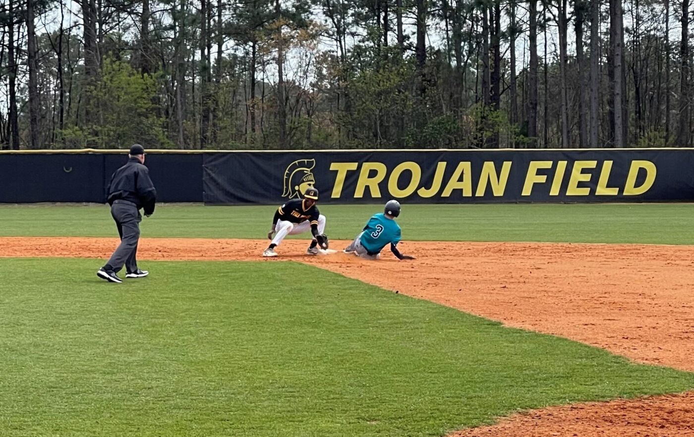 Teammates wait at home plate for a runner to score