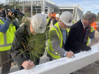 Three men in hard hats sign a steel beam at a construction site.