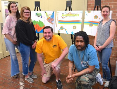 Three people stand and two people kneel in front of poster boards