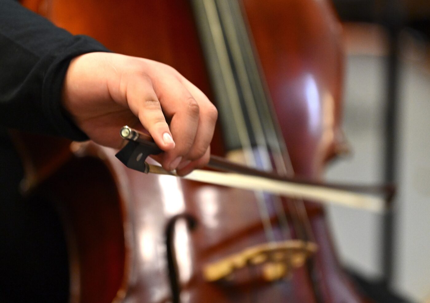 Close up shot of a hand holding a bow on the strings of a cello.