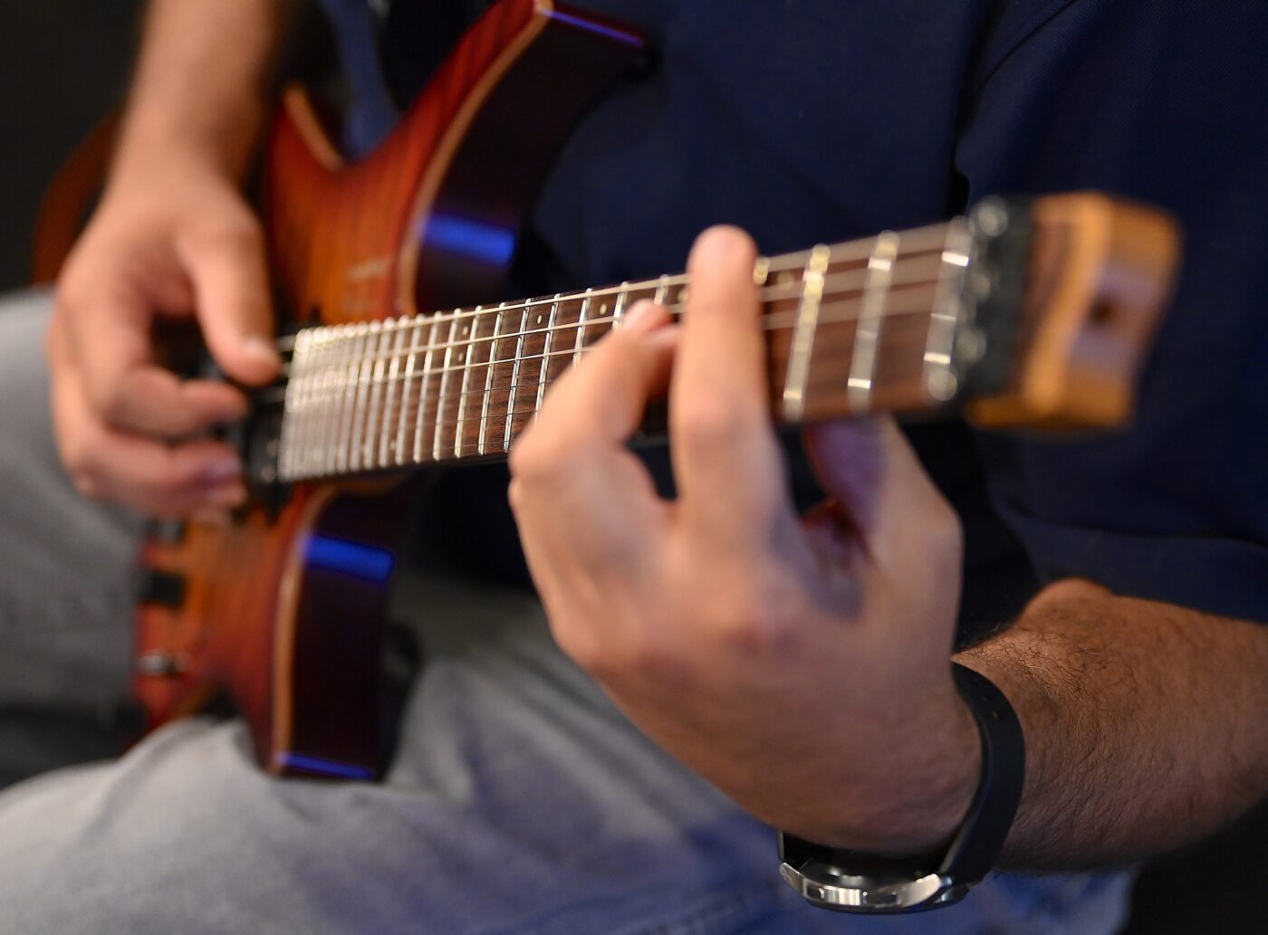 A close up photo of hands playing an electric guitar.