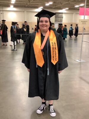 A graduate wearing her cap and gown and a gold stole and medal around her neck poses for the camera.