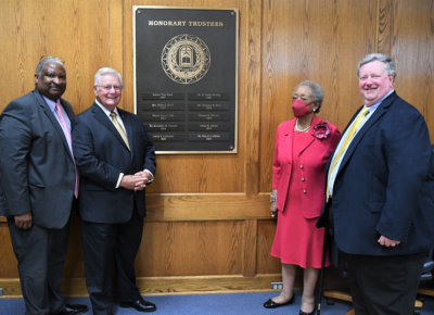 Glenn Adams, Larry Keen, Marye Jeffries and David Williford stand in front of a wall-mounted plaque with the names of the College's Honorary Trustees on it.