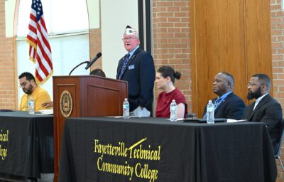 Jessie Bellflowers speaks at a podium. On either side of him, people are seated at tables.