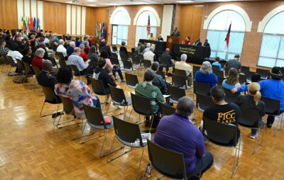 A photo with the back of the crowd gathered to listen to Veterans Day Ceremony speaker Al Lampkins, who is speaking at a podium in the background.