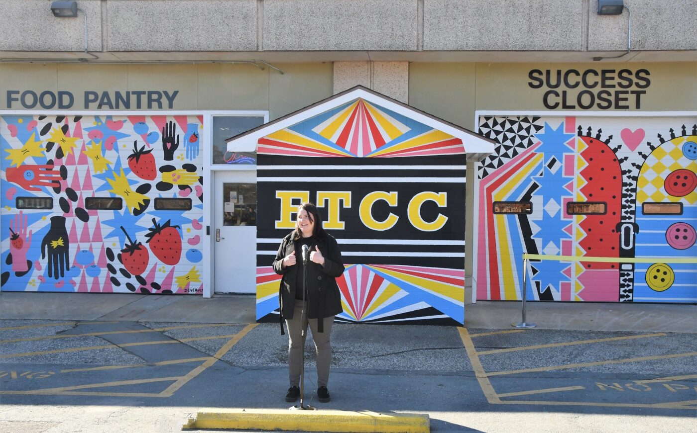 Britney Deveault standings in the parking lot in front of the brightly colored murals she painted on the Food Pantry and Success Closet.