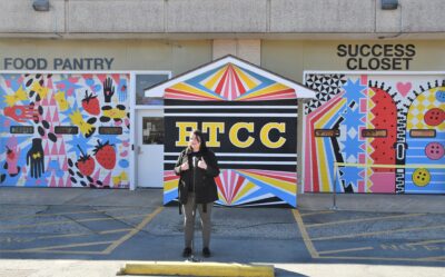 Britney Deveault standings in the parking lot in front of the brightly colored murals she painted on the Food Pantry and Success Closet.