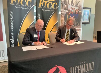 Dale Mcinnis and Mark Sorrells sit at a table and sign paperwork