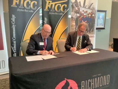 Dale Mcinnis and Mark Sorrells sit at a table and sign paperwork