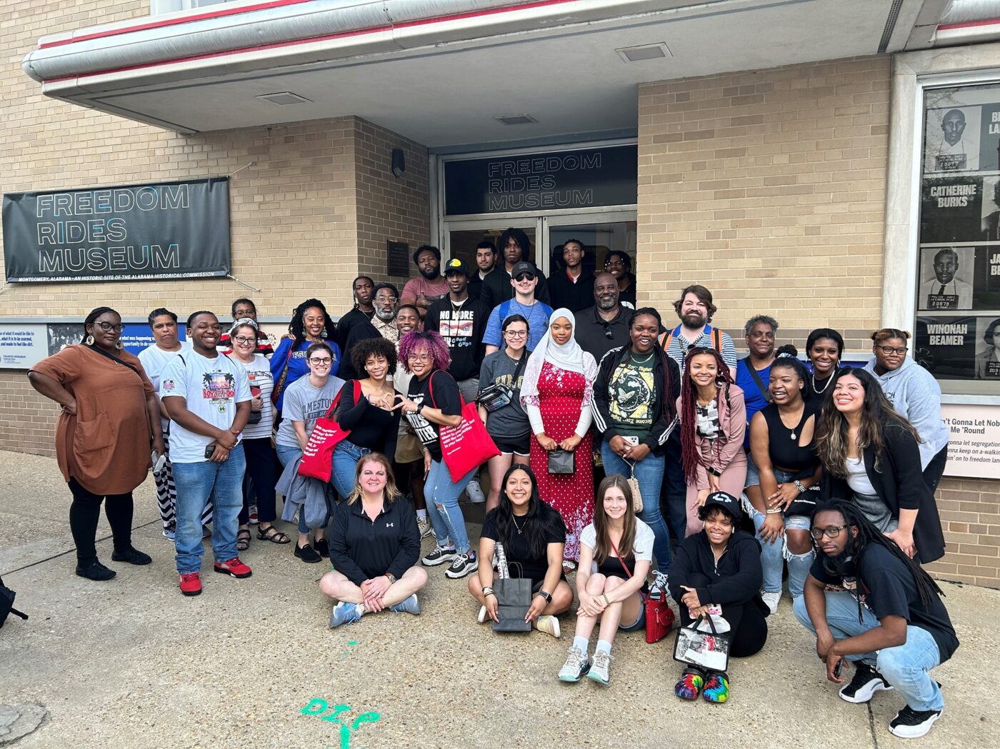 A group of students and chaperones pose for a photo in front of the Freedom Rides Museum.