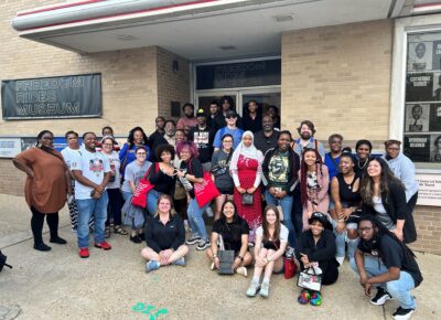 A group of students and chaperones pose for a photo in front of the Freedom Rides Museum.