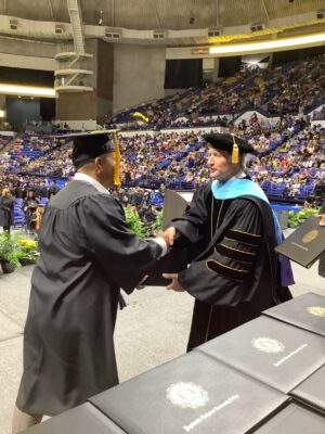 FTCC President Dr. Mark Sorrells shakes hands with a graduate while handing him a diploma folder.