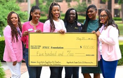 A group of six women stand holding an oversized check written in the amount of $500. 