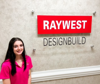 Whitney Carter stands by a logo that says Ray West Design Build