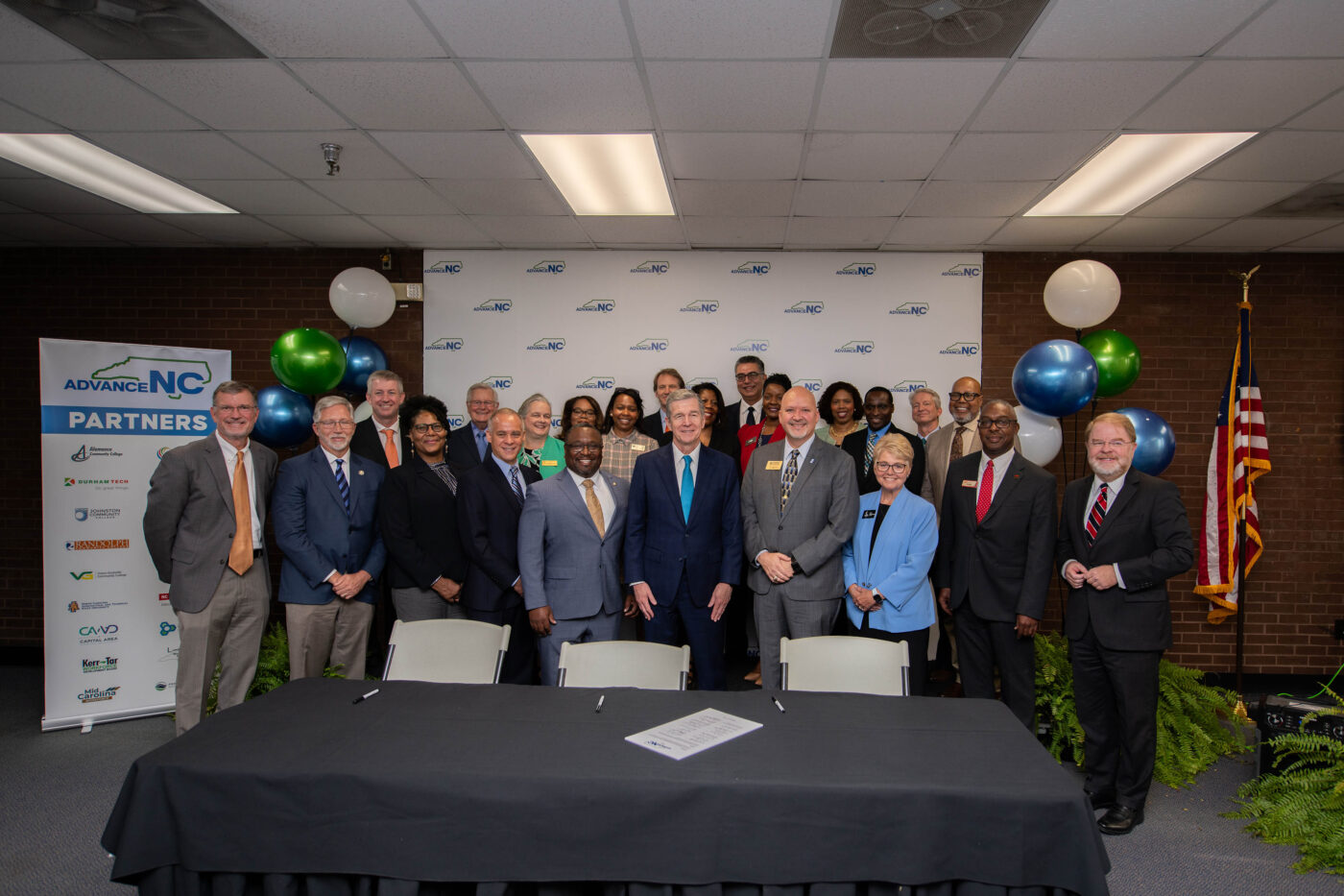 A group of college and workforce development board representatives and Gov. Roy Cooper stand behind a table.