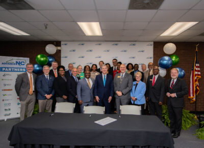 A group of college and workforce development board representatives and Gov. Roy Cooper stand behind a table.