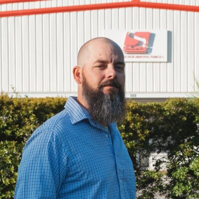 Brandon Meredith, a bald man with a long beard wearing a blue shirt, stands outside.