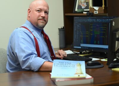 Glenn Massie sits at a desk with the book he illustrated on display in front of him.