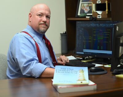 Glenn Massie sits at a desk with the book he illustrated on display in front of him.