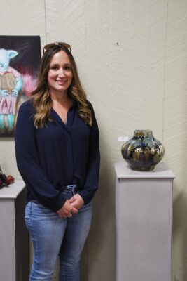 A woman stands next to a ceramic vase that's on top of a podium.