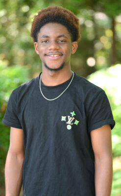 A young man in a black T-shirt stands outside.