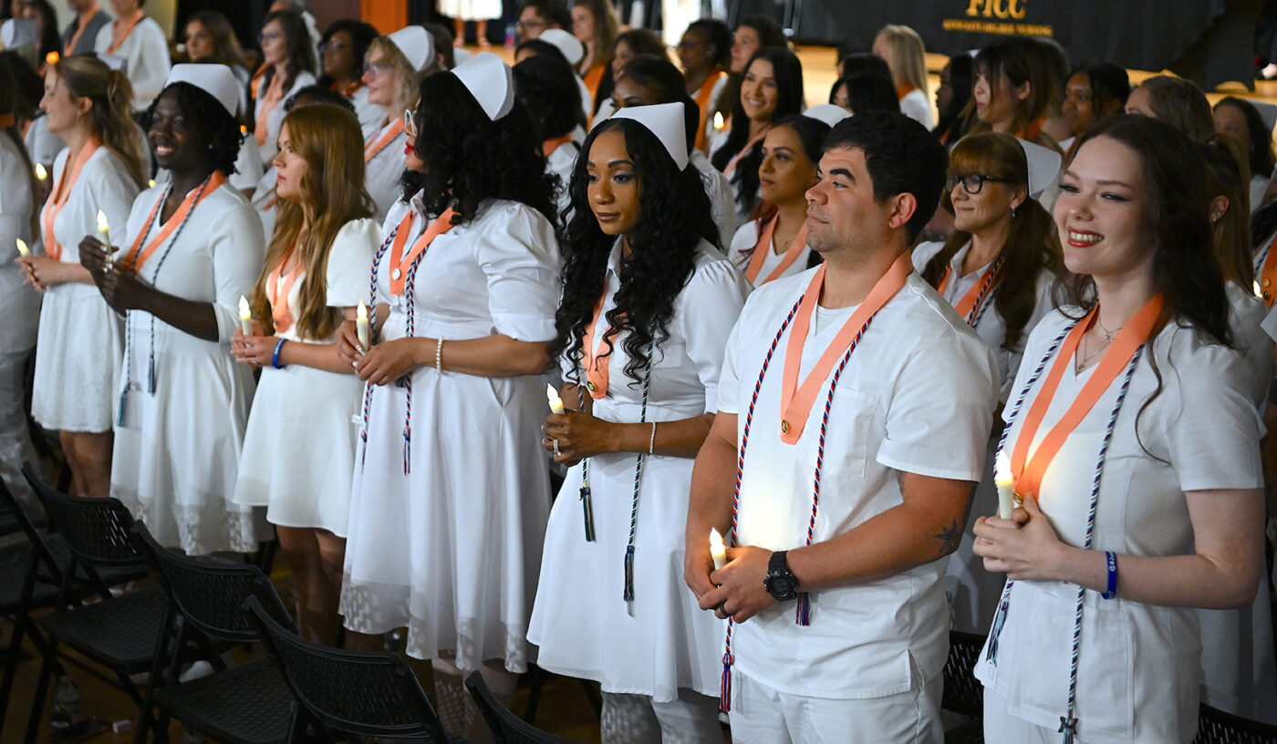 Nursing students in white uniforms hold candles.