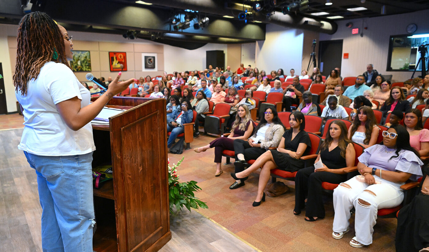 A woman at a podium speaks to a seated audience.