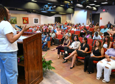 A woman at a podium speaks to a seated audience.