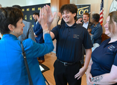 A woman and young man high-five while a young woman looks on.