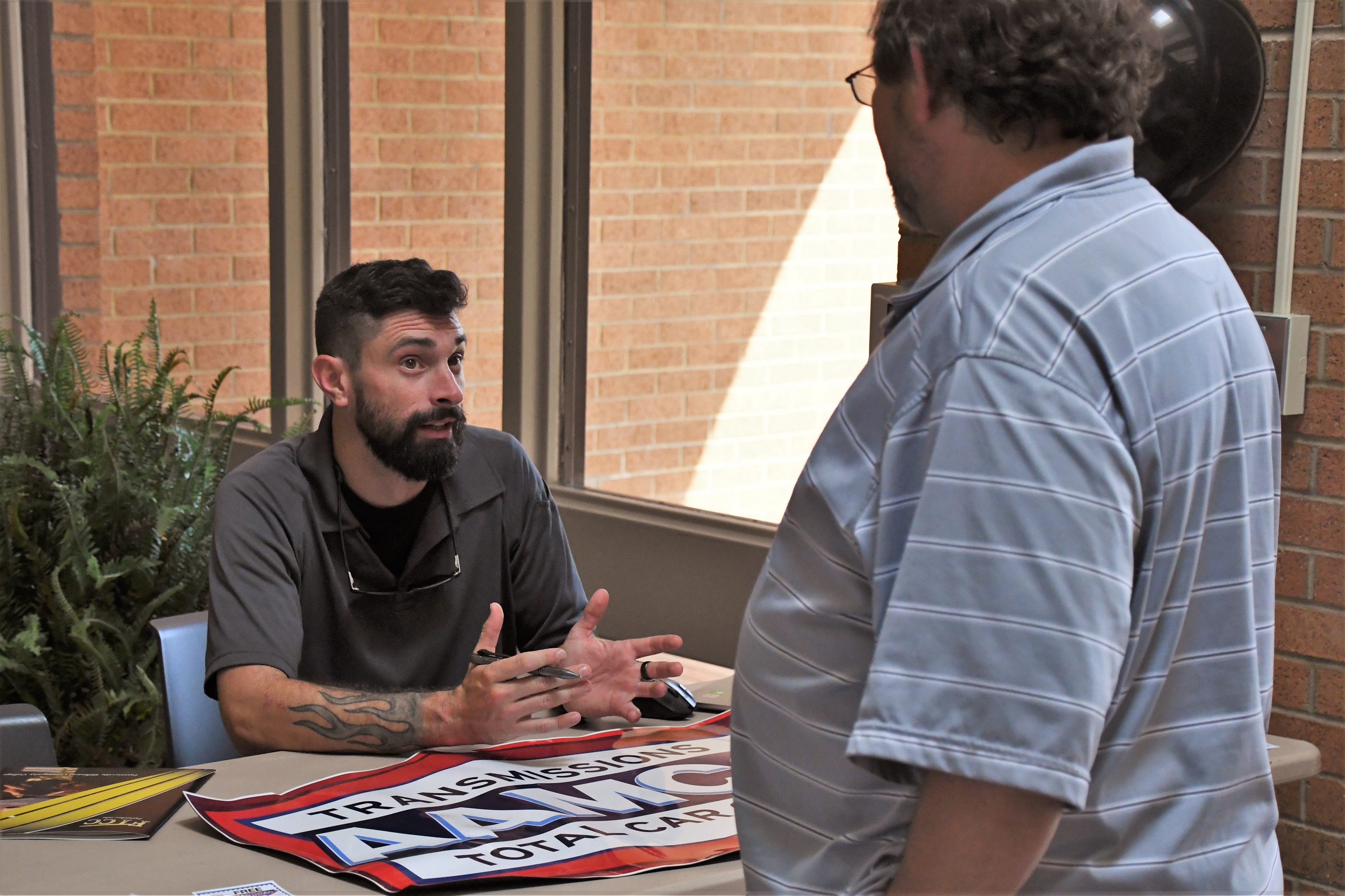 An employer sits at a table while talking with a job seeker standing in front of the table.