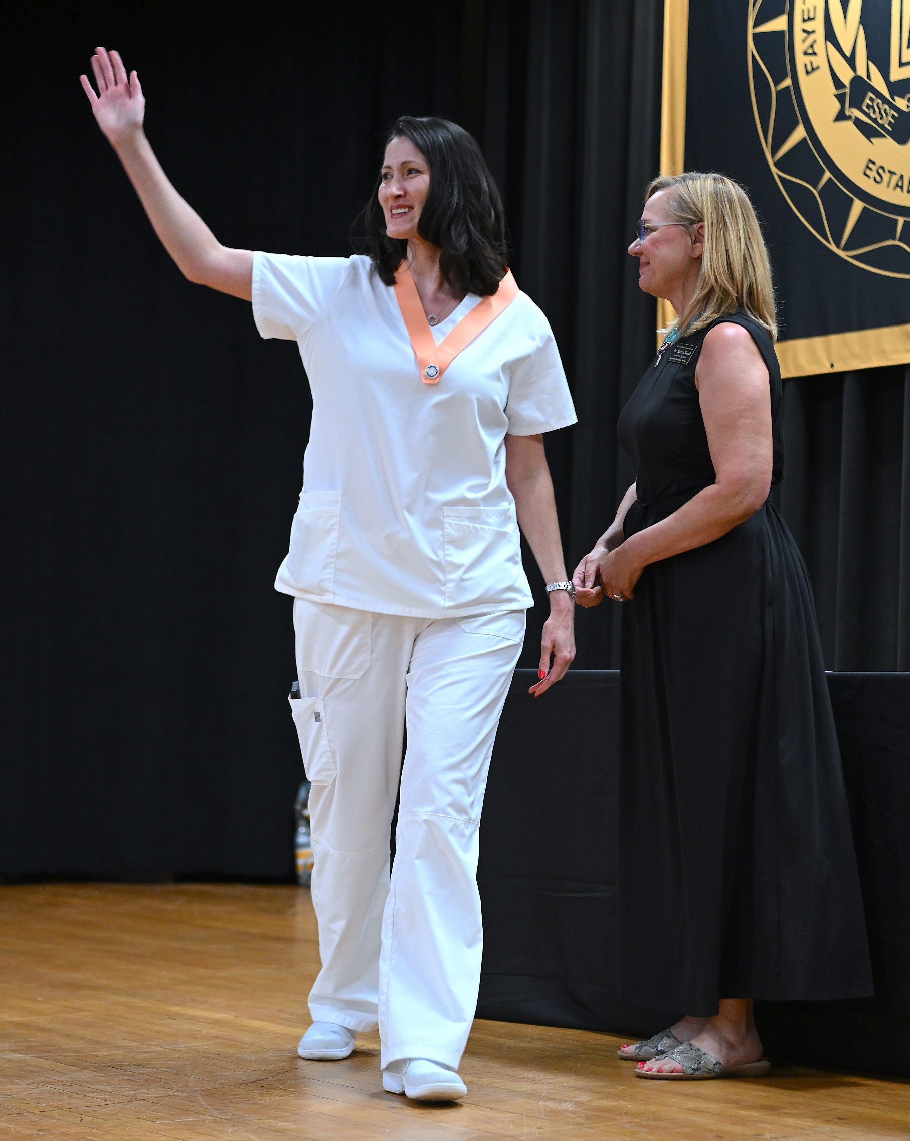 A graduate waves after receiving her pin. Dr. Murtis Worth stands next to her.