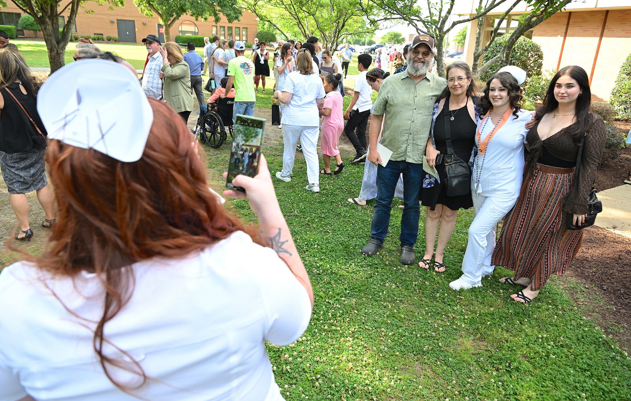 A photo taken from behind a Nursing graduate who is taking a photo of another Nursing graduate and her family.