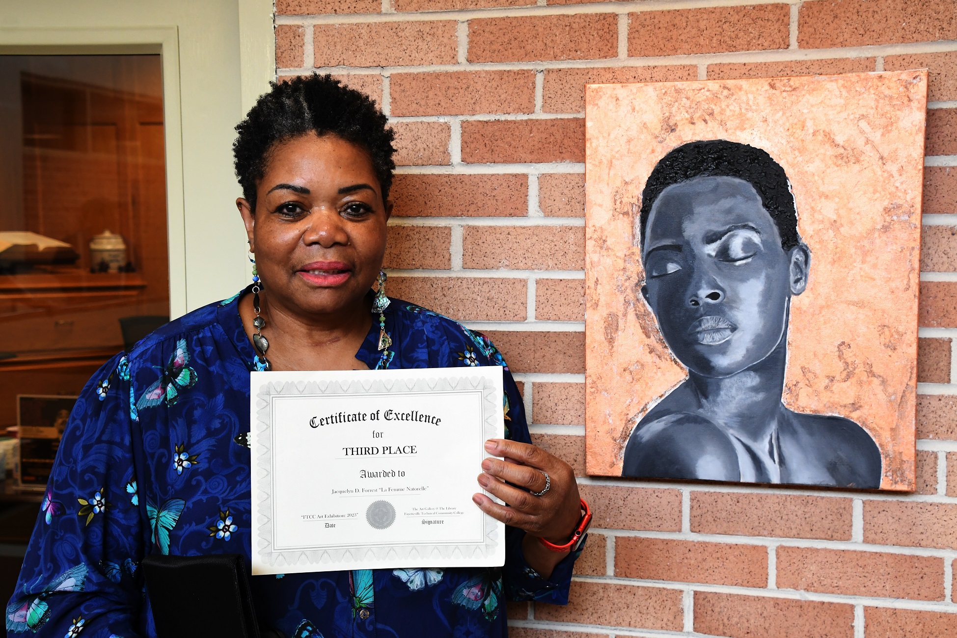 Jacquelyn D. Forrest stands beside her artwork, "La Femme Natorelle," and holds her third-place certificate.