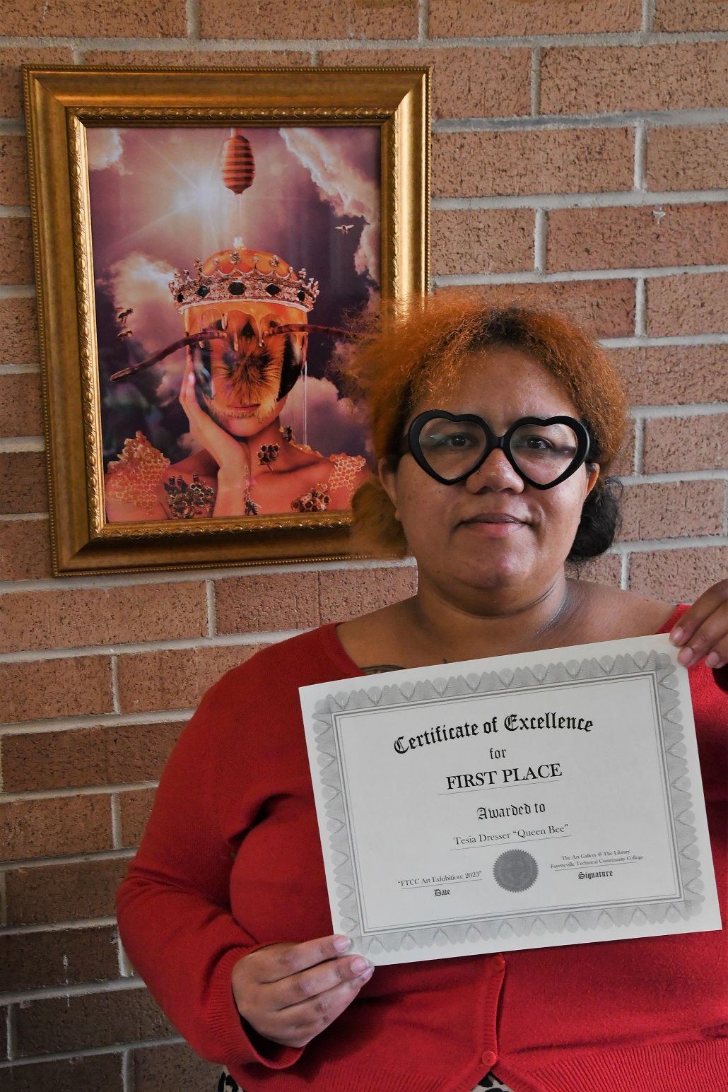 Tesia Dresser stands in front of her artwork, "Queen Bee," and holds her first-place certificate.