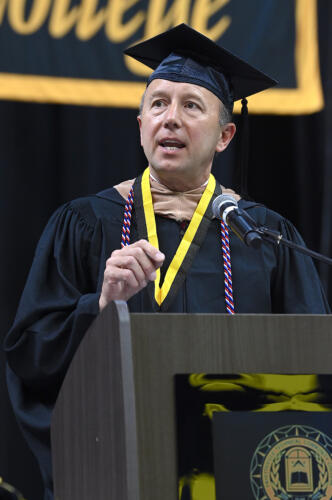 Mike Nagowski, dressed in graduation regalia, speaks at the podium.