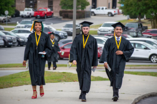 Three graduates walk up a slightly inclined sidewalk. 