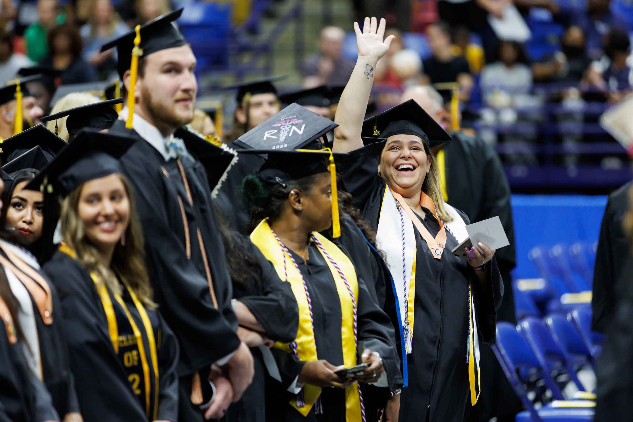 A graduate extends her arm over her head to wave as she waits to take her seat.