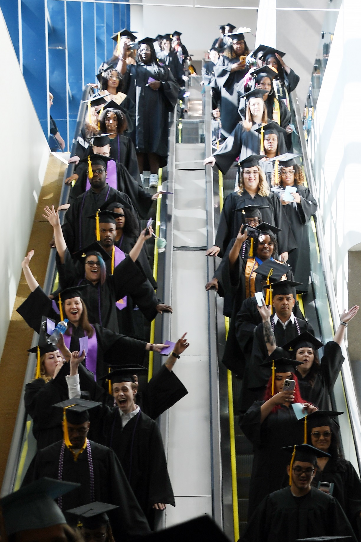 Graduates line two escalators side-by-side.