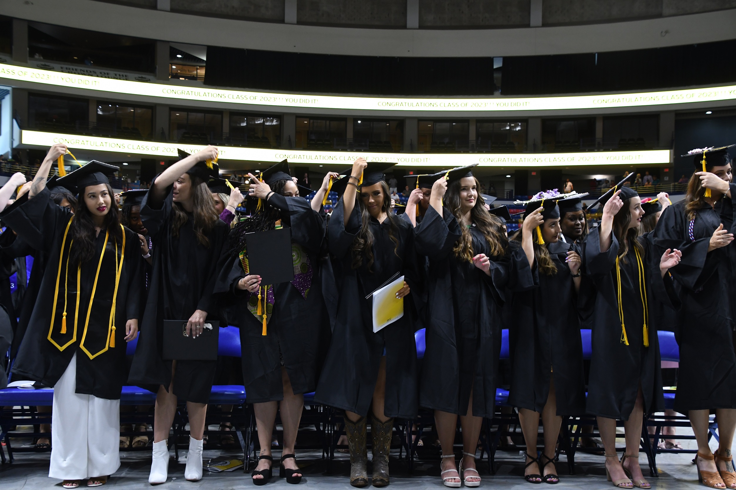 Graduates stand up and reach for their tassels.