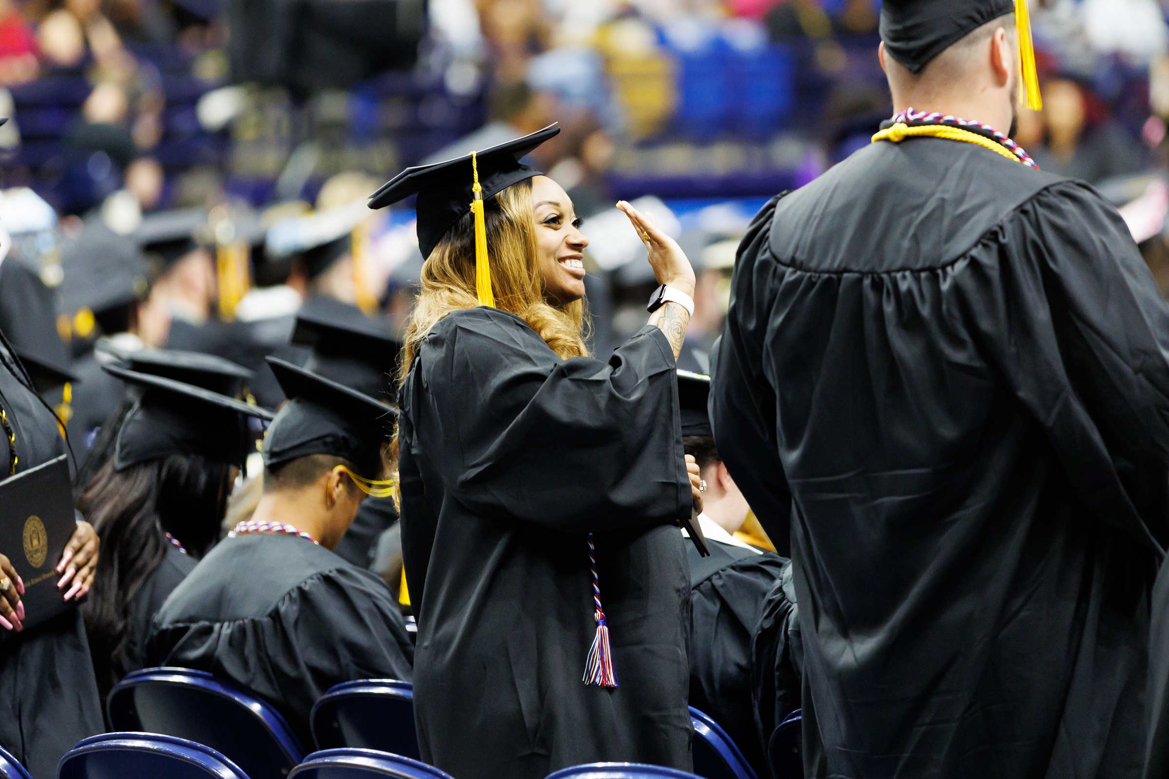 A graduate, shown in profile, smiles and waves at the crowd.