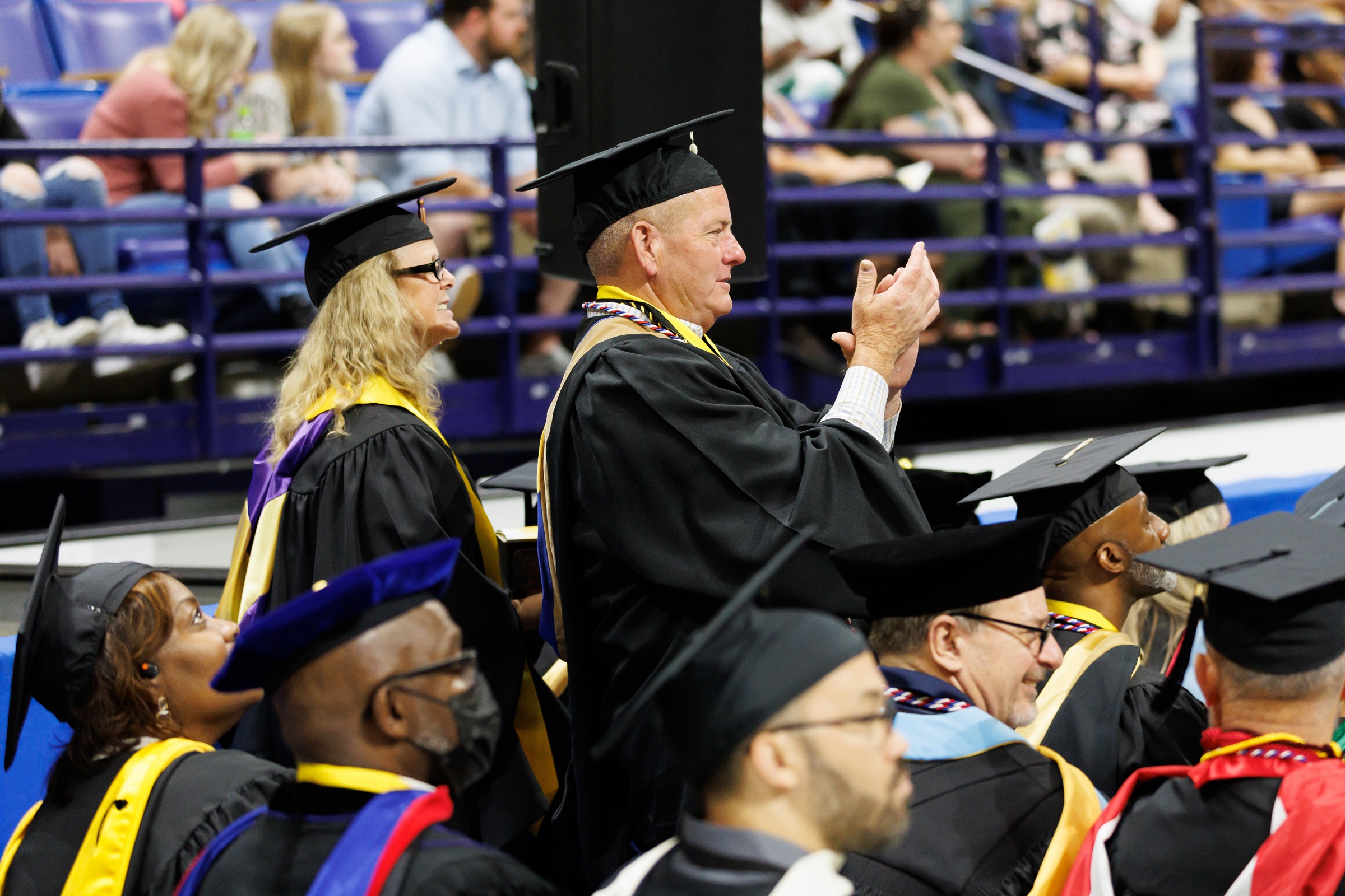 Two faculty members, shown in profile, stand and clap.