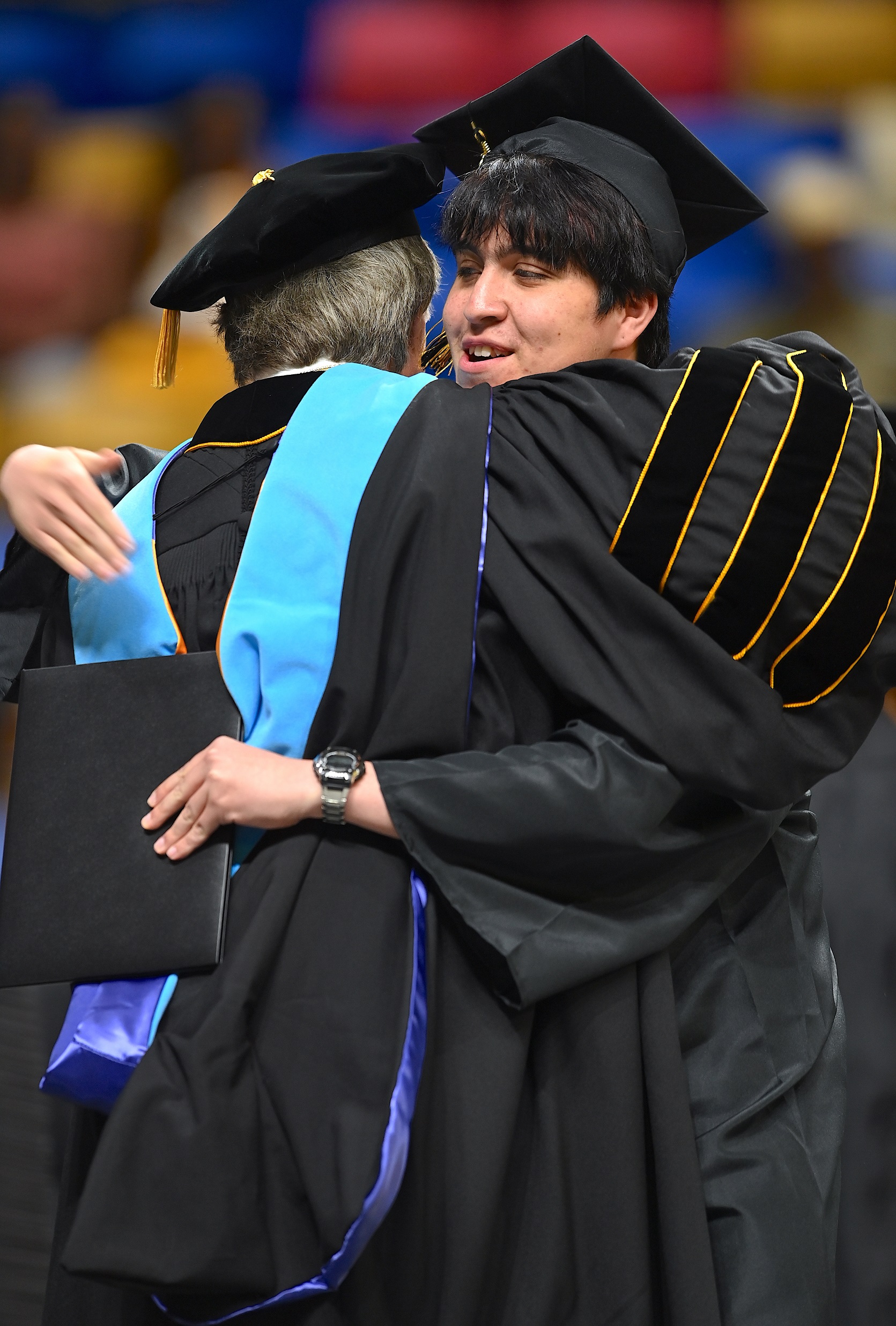 A graduate with short black hair hugs Dr. Mark Sorrells after receiving his diploma folder. 