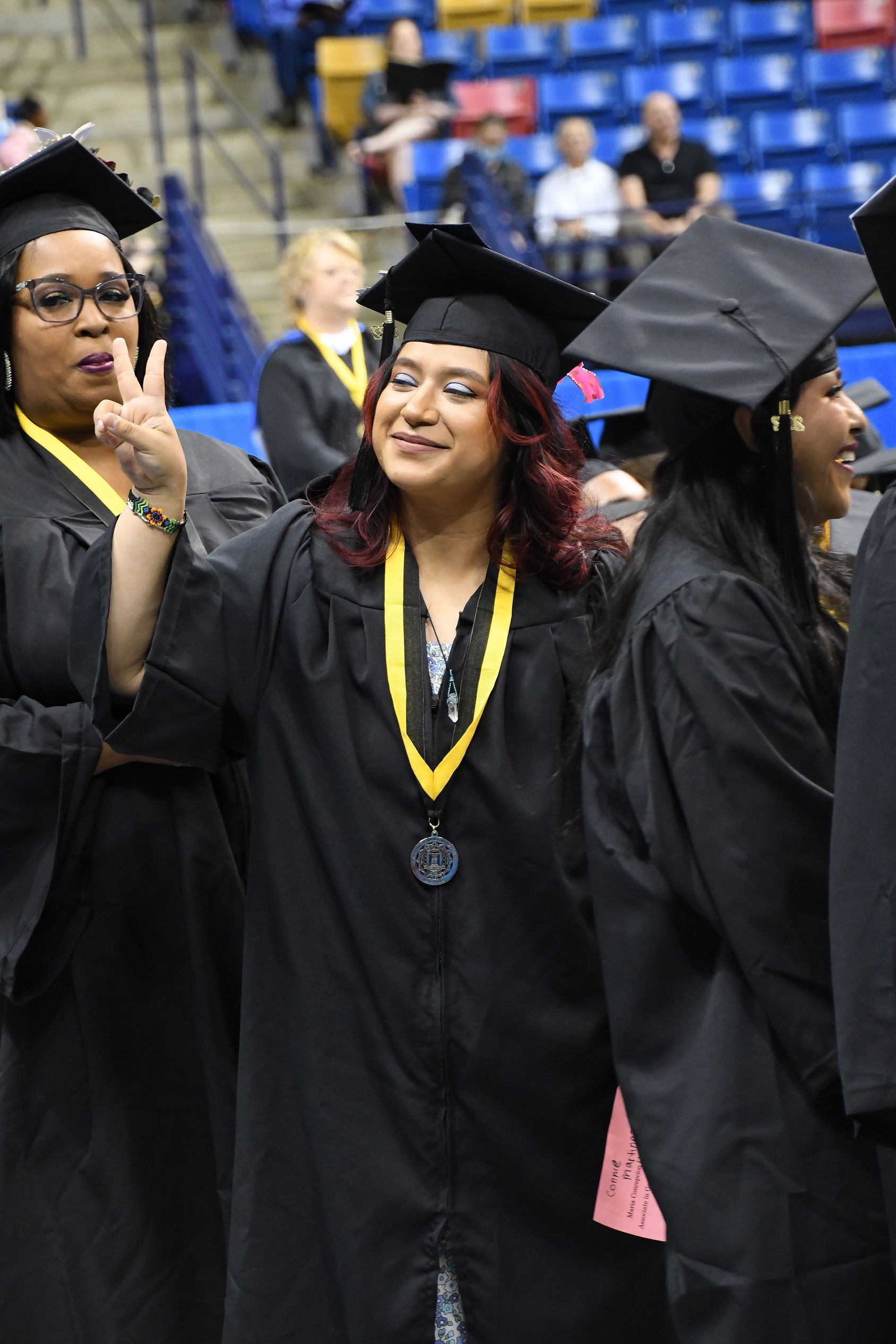 A graduate holds up two fingers in a peace sign directed at the crowd.