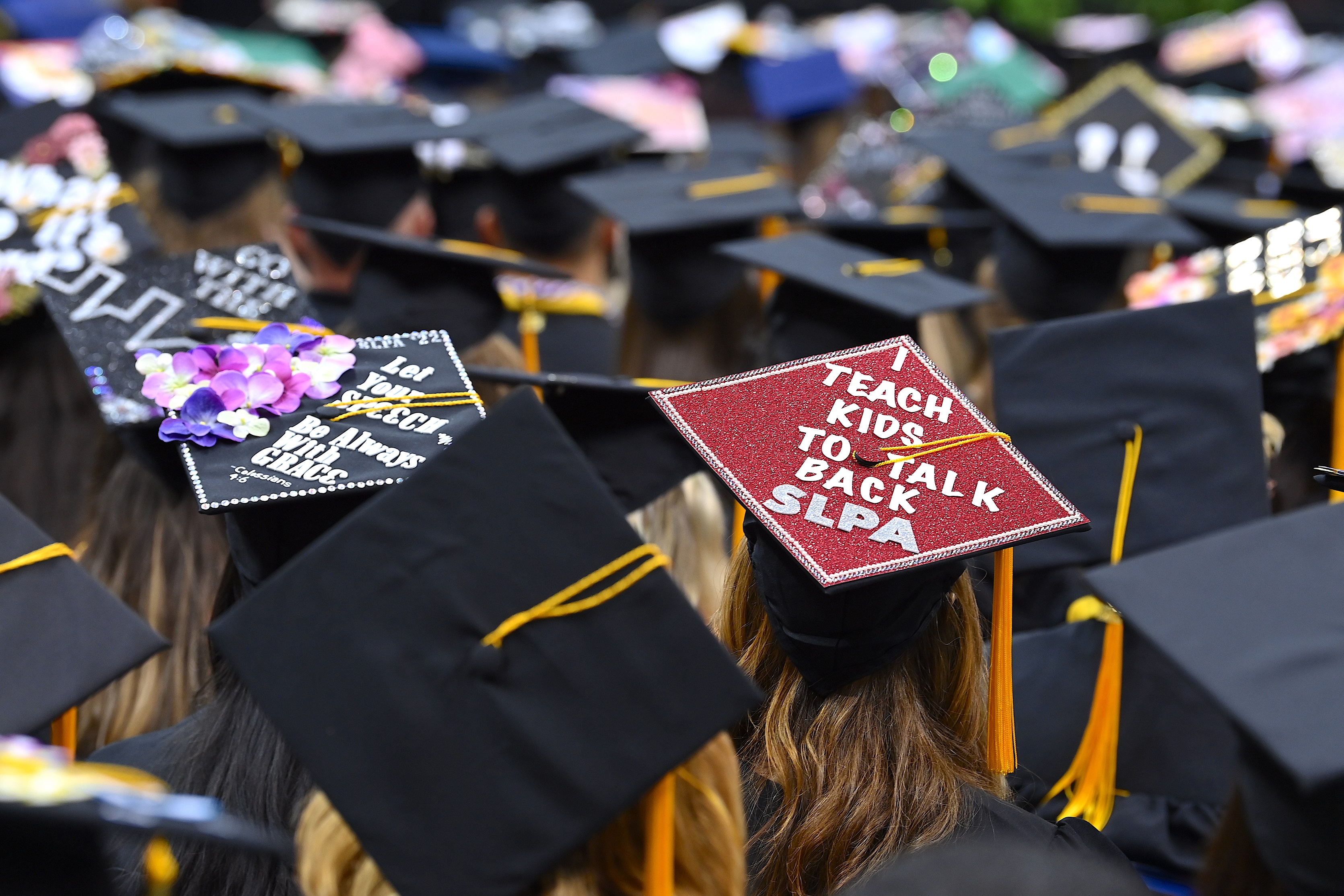 Two decorated graduation caps. The one on the left says "Let you speech be always with grace. Colossians 4:6." The on on the right says "I teach kids to talk back. SLPA."