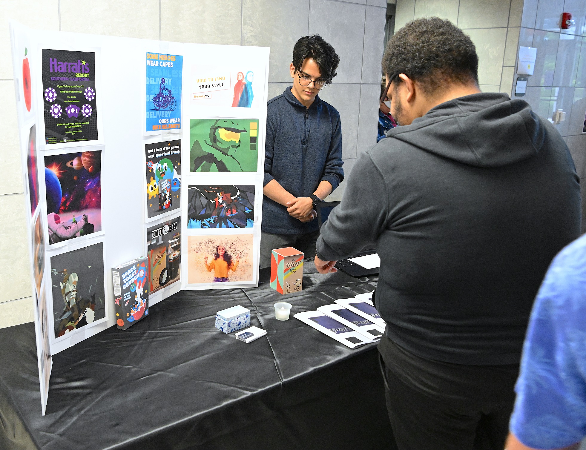 A graduate stands behind a table where his trifold poster board stands.